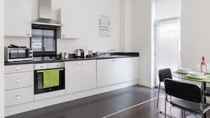 A modern kitchen with white cabinets, a stainless steel range hood, a microwave, and a built-in oven. There is a black countertop, a green towel hanging from the oven handle, and a wall-mounted light. - 2bed Apt -king Bed -free Parking - Family Friendly (Birmingham)