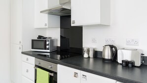 A modern kitchen with white cabinets, a black countertop, a microwave, a kettle, and a toaster. - 2bed Apt -king Bed -free Parking - Family Friendly (Birmingham)