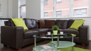 A modern living room with a brown leather sofa, green cushions, a glass coffee table, and a potted plant. - 2bed Apt -king Bed -free Parking - Family Friendly (Birmingham)
