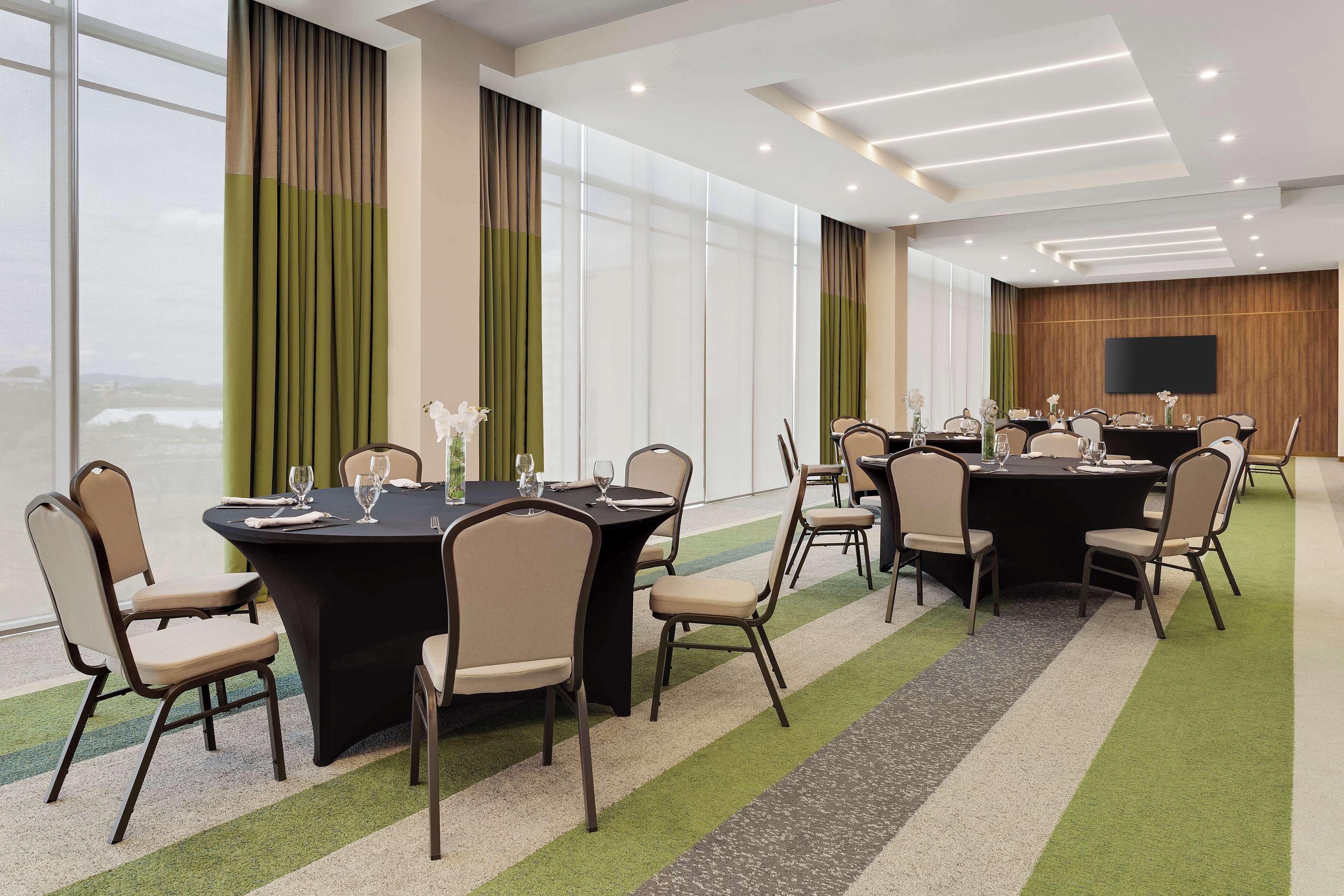 A conference room with multiple tables and chairs, large windows, and a flat-screen TV on the wall.