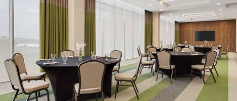 A conference room with multiple tables and chairs, large windows, and a flat-screen TV on the wall.