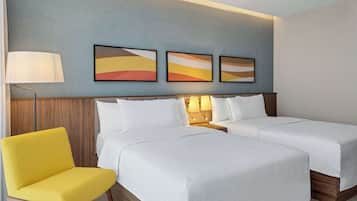 A hotel room with two beds, a yellow chair, and three abstract paintings on the wall.