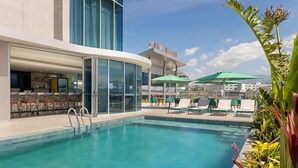 A pool area with lounge chairs and umbrellas, a bar, and a 'City Mall' sign. - Hilton Garden Inn San Jose Airport City Mall (Alajuela)