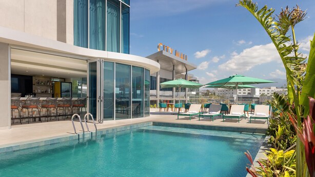 A pool area with lounge chairs and umbrellas, a bar, and a 'City Mall' sign. - Hilton Garden Inn San Jose Airport City Mall (Alajuela)