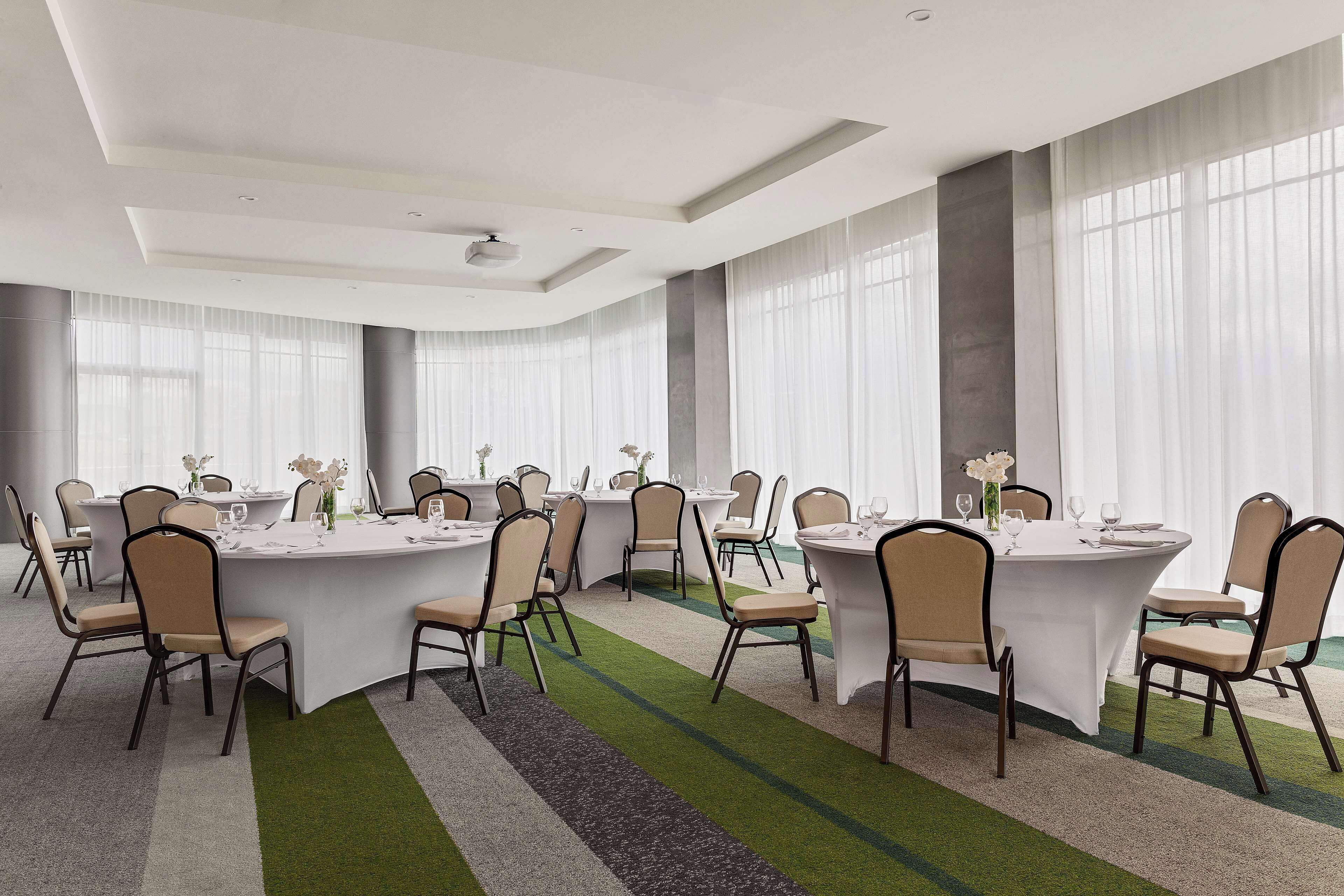 A conference room with round tables, beige chairs, and a green carpet.