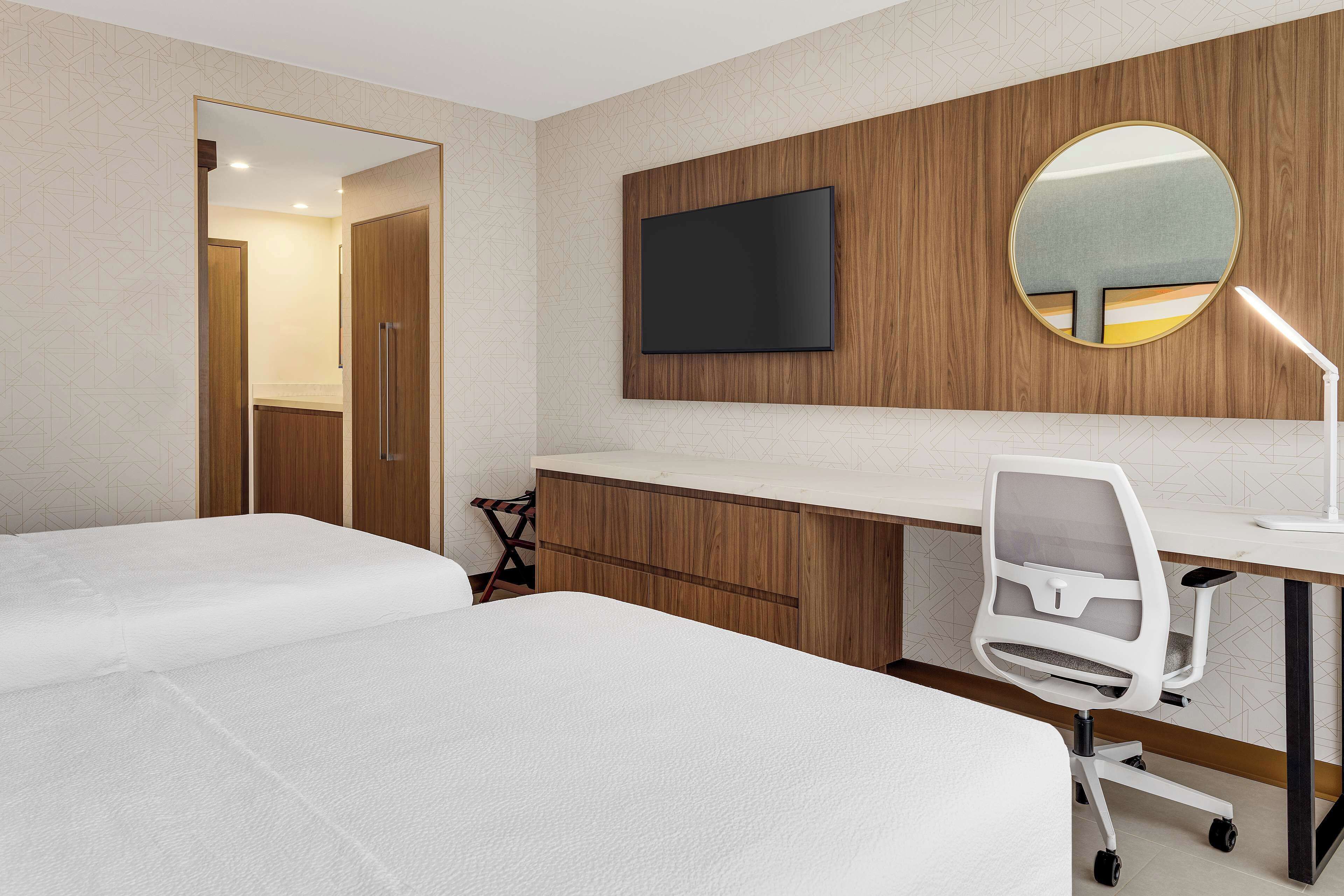 A hotel room with two beds, a desk with a computer, a chair, a TV mounted on the wall, and a mirror.