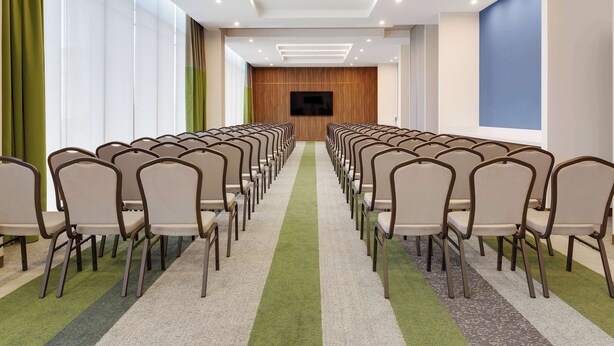 A conference room with rows of chairs, a large screen, and a carpeted floor. - Hilton Garden Inn San Jose Airport City Mall (Alajuela)