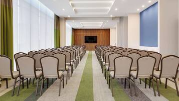 A conference room with rows of chairs, a large screen, and a carpeted floor.