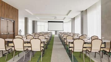 A conference room with rows of tables and chairs, a projector screen, and a carpeted floor.