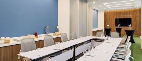 A conference room with long tables, chairs, and a TV screen.