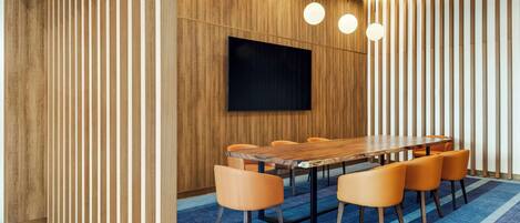 Una sala de conferencias moderna con pared de paneles de madera, un televisor de pantalla plana grande, una mesa de madera y sillas anaranjadas.