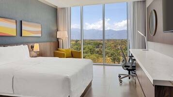Habitación de hotel con una cama grande, un escritorio, una silla y vistas a las montañas.