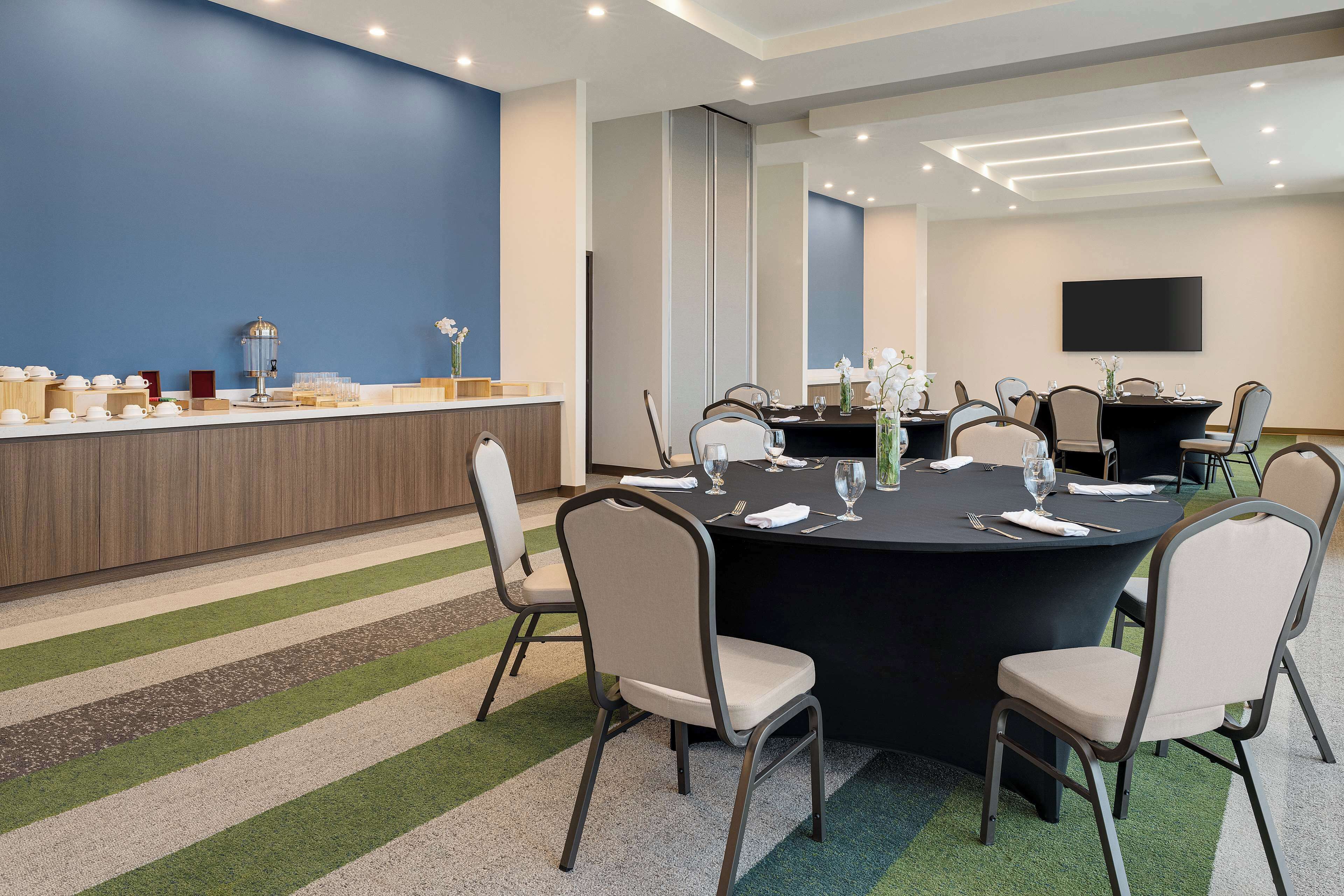 A conference room with a round table, six chairs, a buffet counter, and a flat-screen TV on the wall.