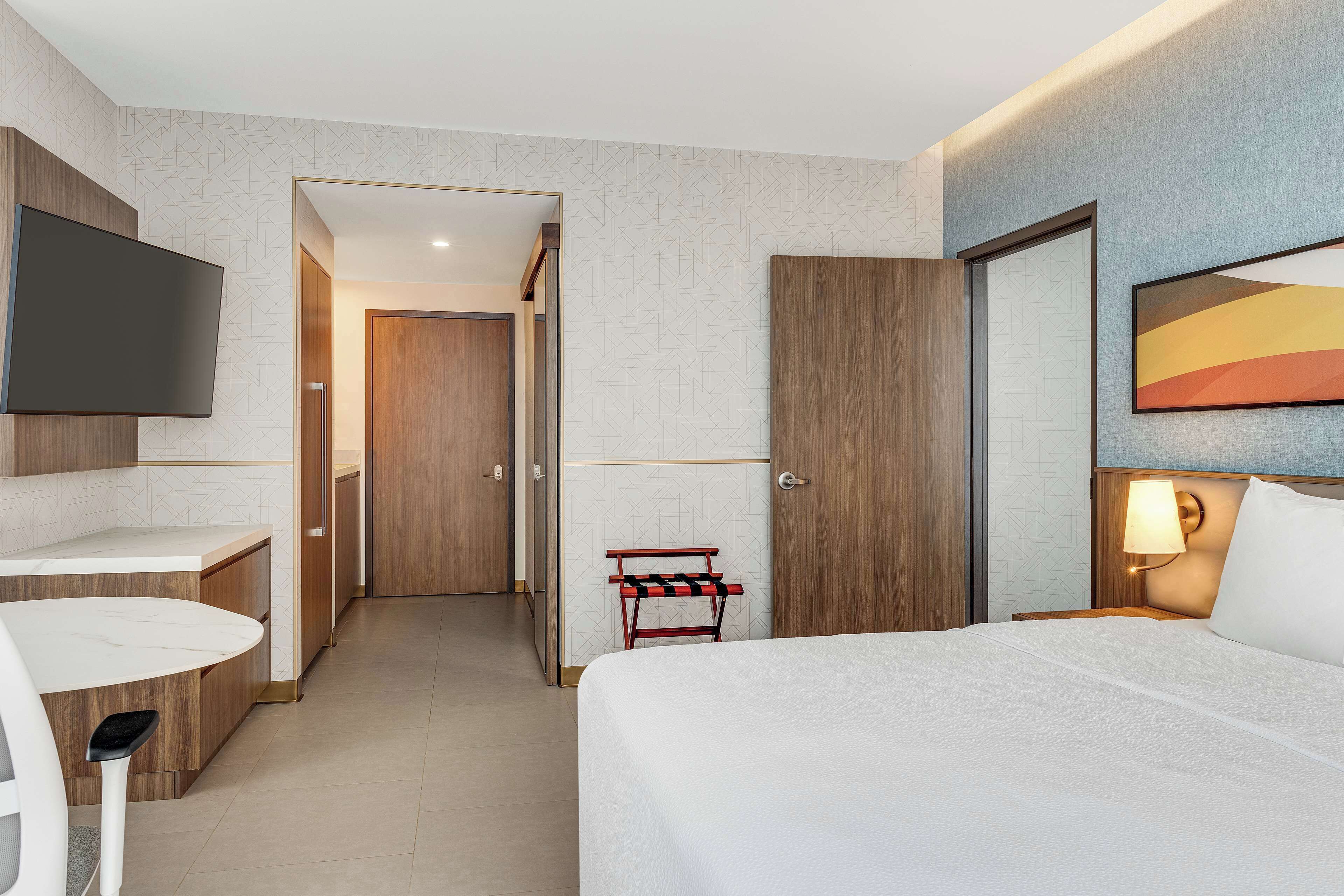 A hotel room with a bed, a desk, a TV, and a door leading to a hallway.