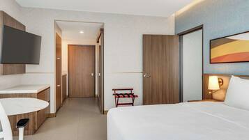 A hotel room with a bed, a desk, a TV, and a door leading to a hallway.
