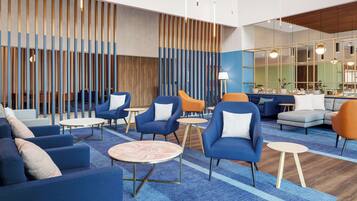 A modern lounge area with blue and orange seating, round tables, and a wooden slatted wall.