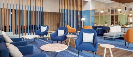 A modern lounge area with blue and orange seating, round tables, and a wooden slatted wall.