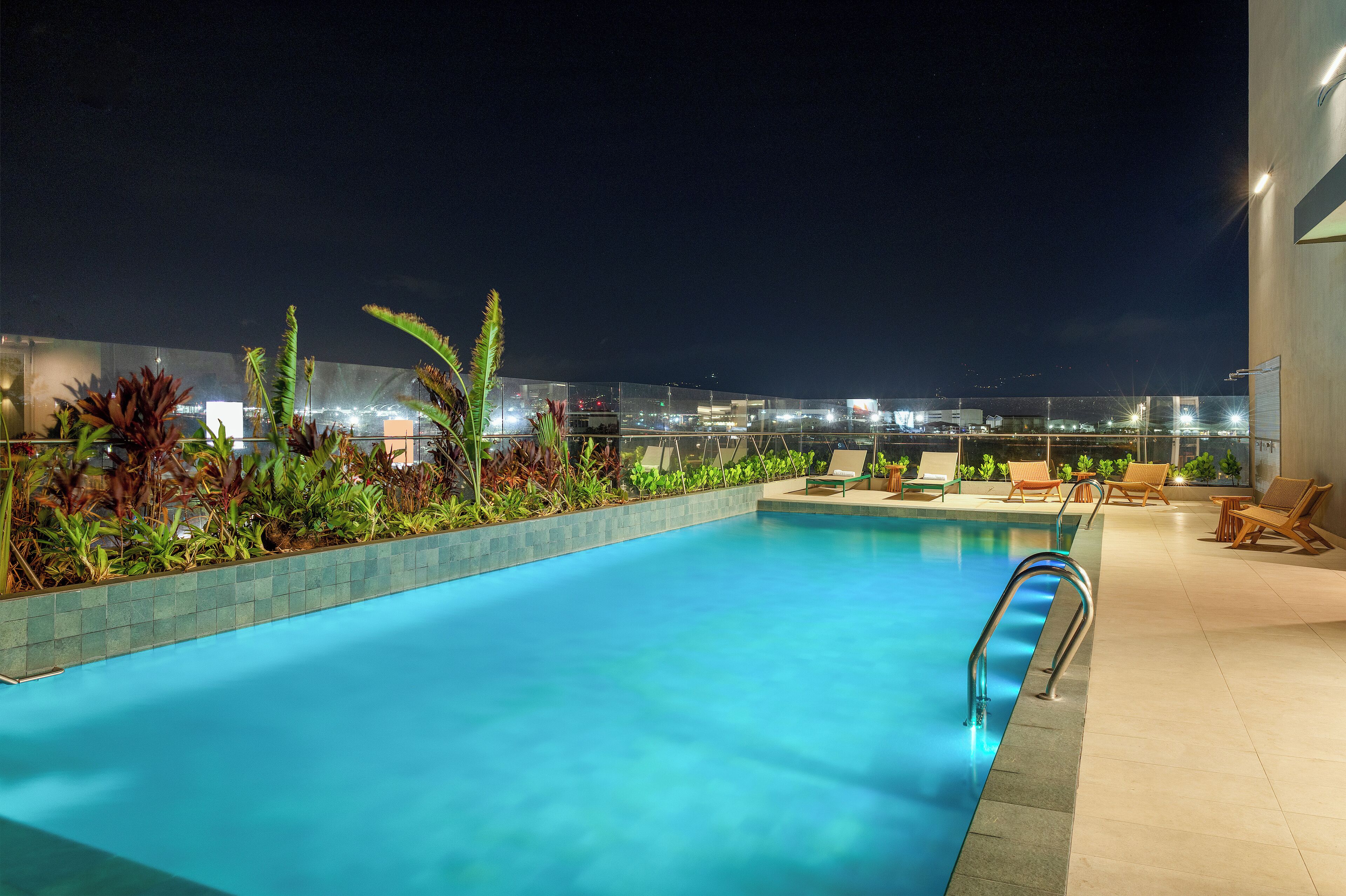 A rooftop pool with clear blue water, surrounded by plants and lounge chairs.