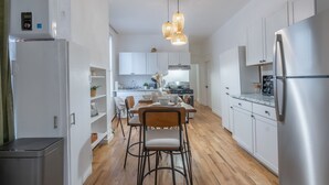 A modern kitchen with white cabinets, stainless steel appliances, a dining area with a wooden table and chairs, and a pendant light fixture.