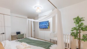A bedroom with a bed, a desk, a chair, a television, and a potted plant.