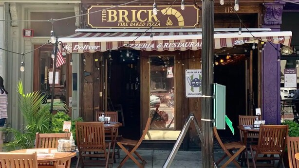 A brick building with a sign reading "The Brick Fire Baked Pizza."