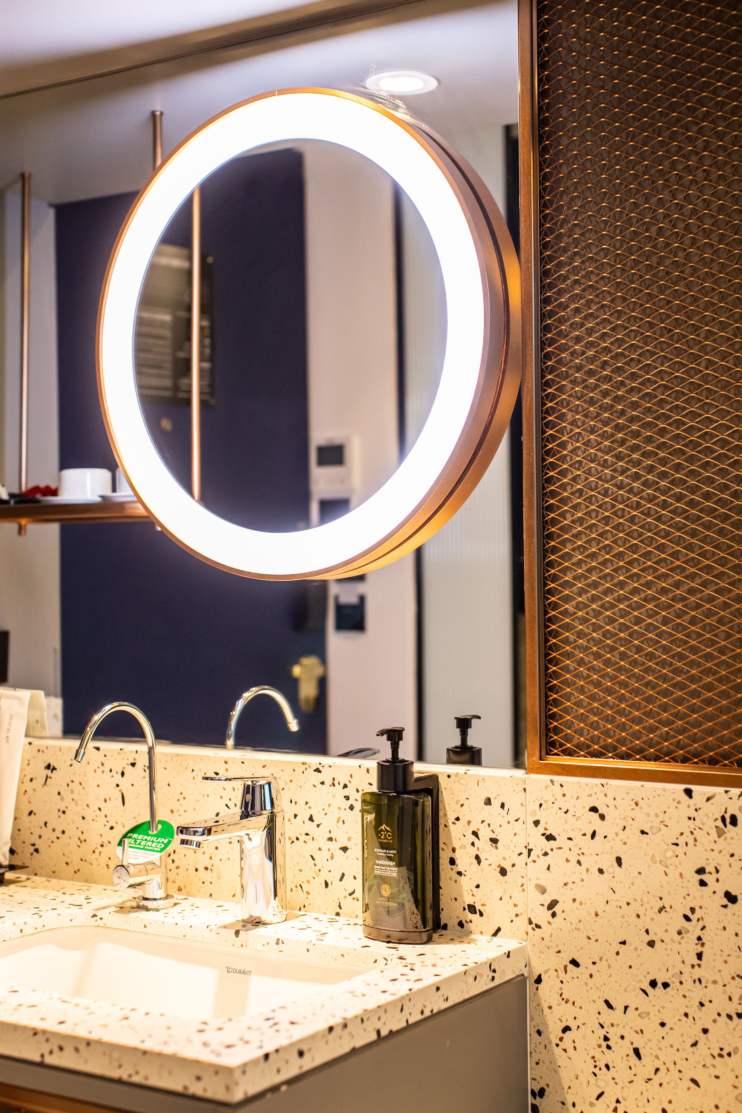 A bathroom with a round mirror, a sink, and a soap dispenser.