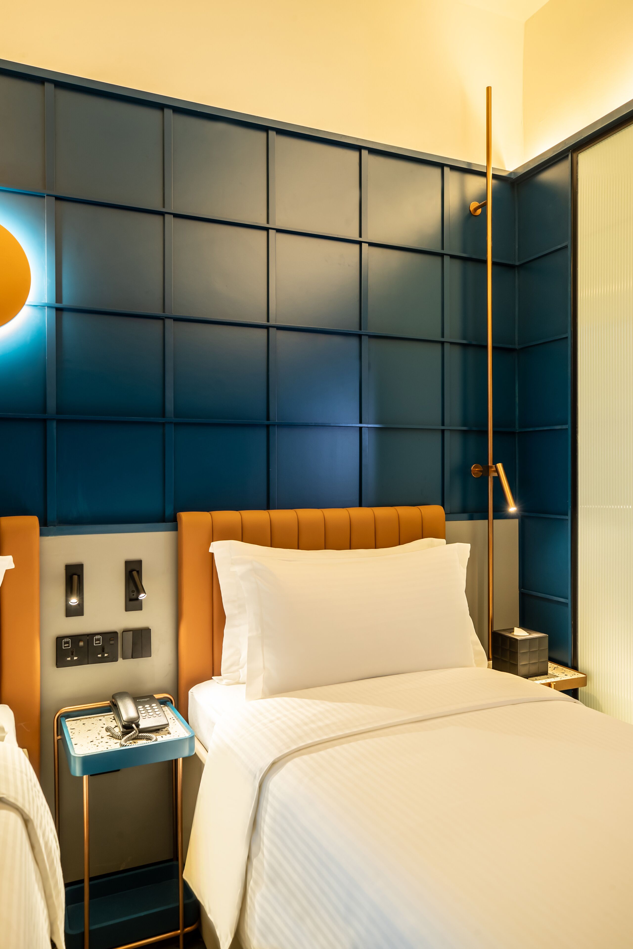 A hotel room with a large bed, a bedside table with a phone, and a wall-mounted light fixture.