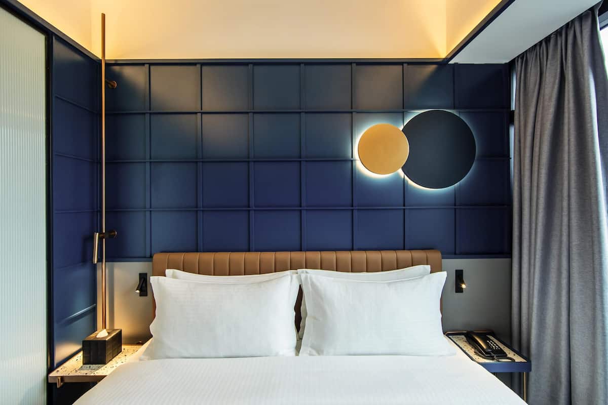 Una habitación de hotel con cama, mesitas de noche, una lámpara de pared y un aplique circular.