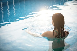 Une personne dans une piscine dont l’eau est claire et où la lumière du soleil se reflète à la surface.