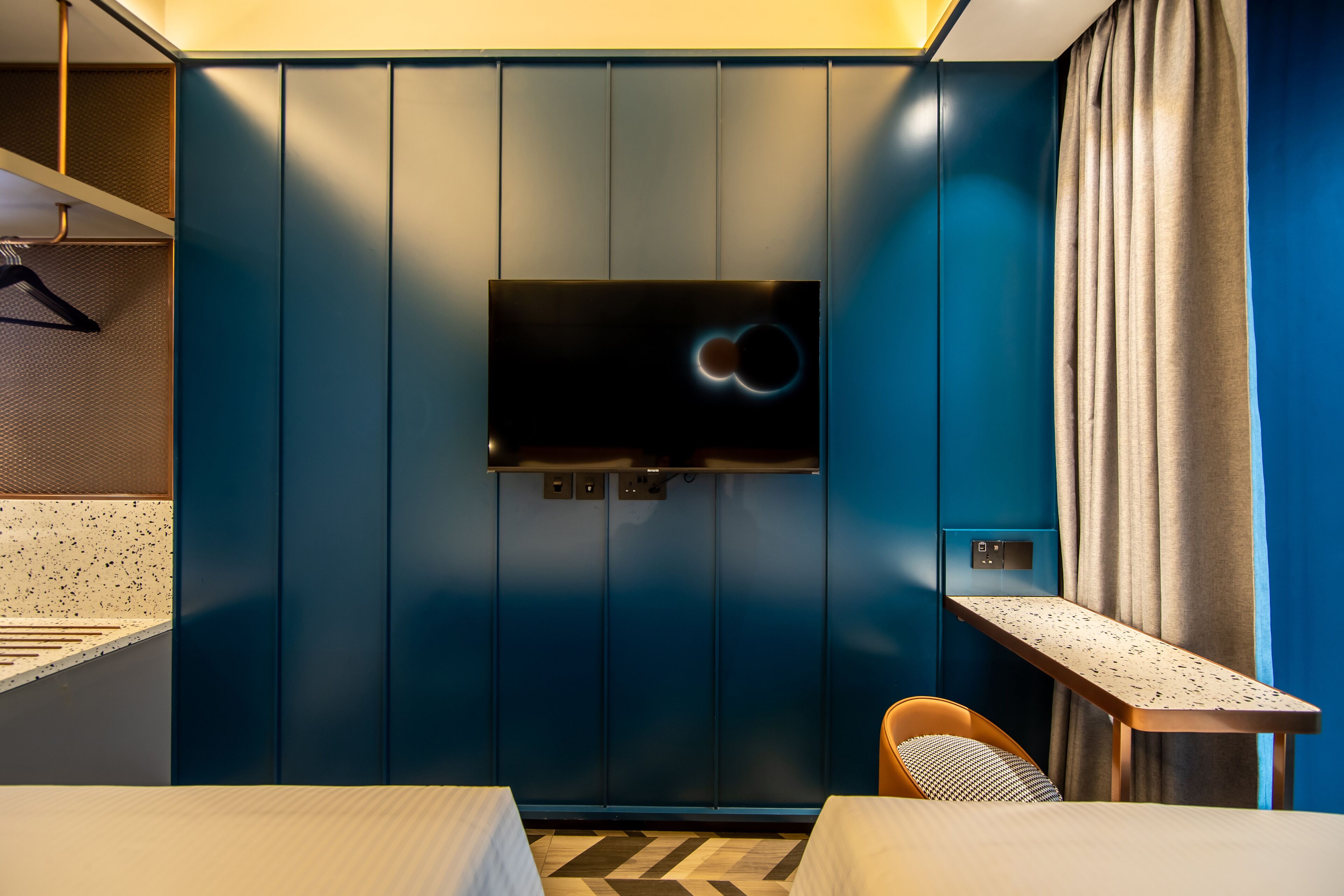 Een hotelkamer met een bed, een bureau, een stoel, een aan de muur bevestigde televisie en een gordijn.
