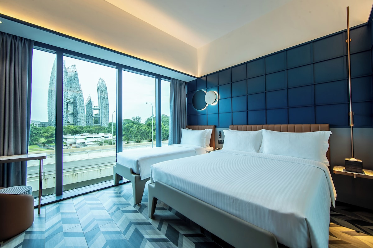 A modern hotel room with two beds, large windows, a view of city buildings, and a blue accent wall.
