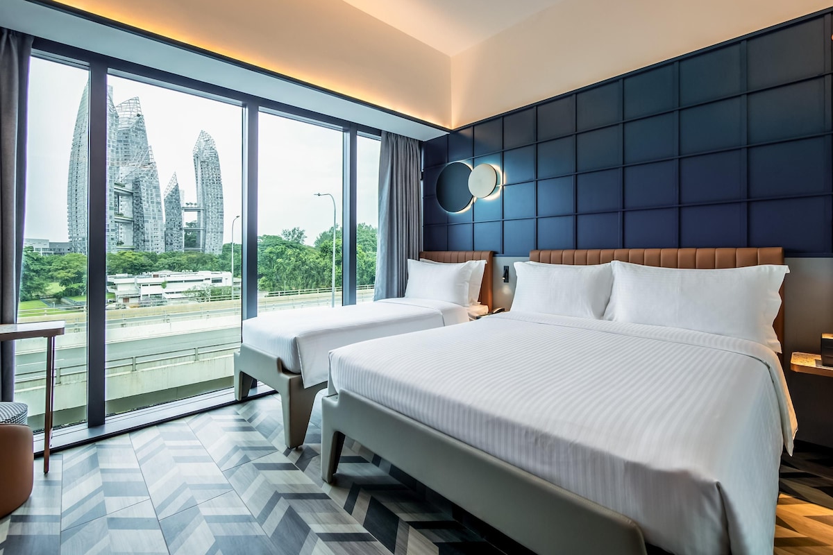 Habitación de hotel con dos camas, ventanas amplias, vistas a edificios de la ciudad y un diseño moderno.