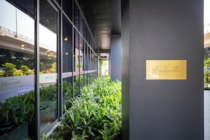A modern hotel corridor with glass walls, indoor plants, and a sign reading "Handwritten Collection".