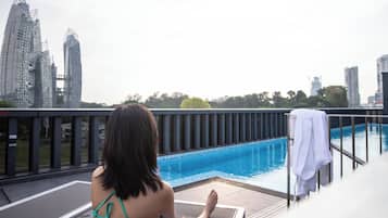 A woman in a green bikini sitting by a pool with a cityscape in the background.