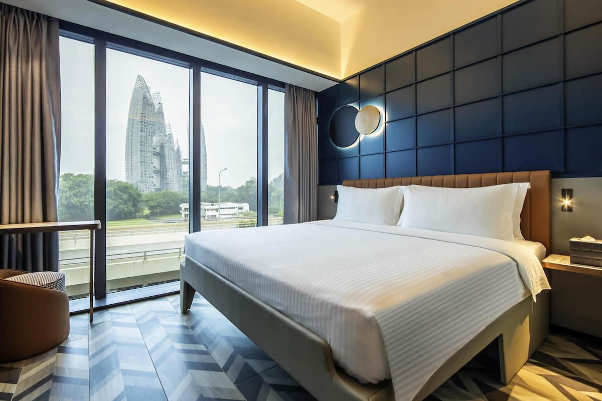 Una habitación de hotel moderna con una cama grande, vistas a un paisaje urbano y un ventanal amplio.