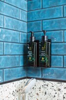 Two bottles of shower gel on a blue-tiled wall.
