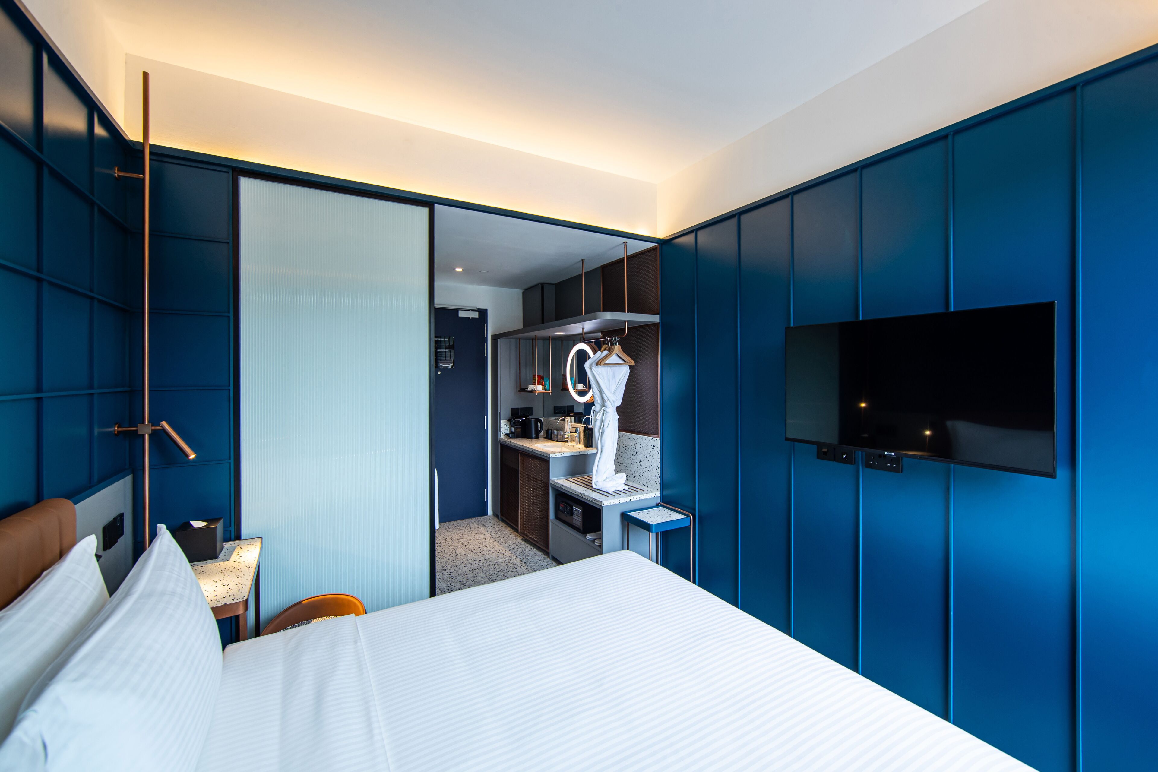 A modern hotel room with a bed, a desk, a mirror, a TV, and a wardrobe.