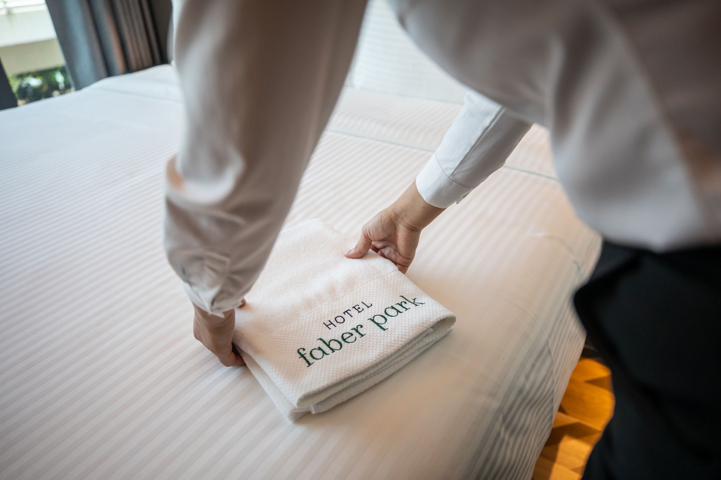 A neatly folded towel with "HOTEL FABER PARK" text on a bed.