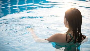 Eine Person in einem Schwimmbecken mit klarem Wasser und Sonnenlichtreflexionen auf der Oberfläche.