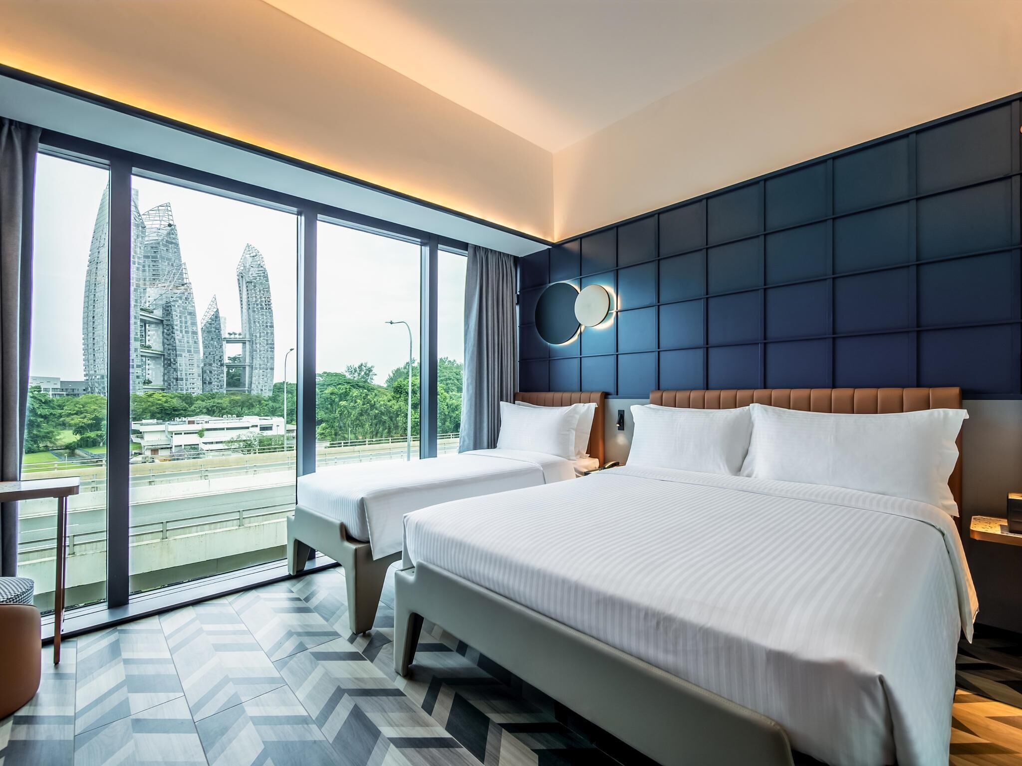 Habitación de hotel con dos camas, ventanas amplias, vistas a edificios de la ciudad y un diseño moderno.