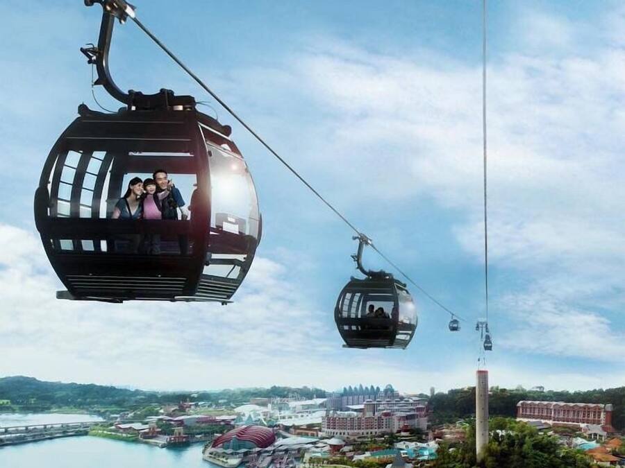 A cable car system with passengers, a body of water, and a distant cityscape with buildings.