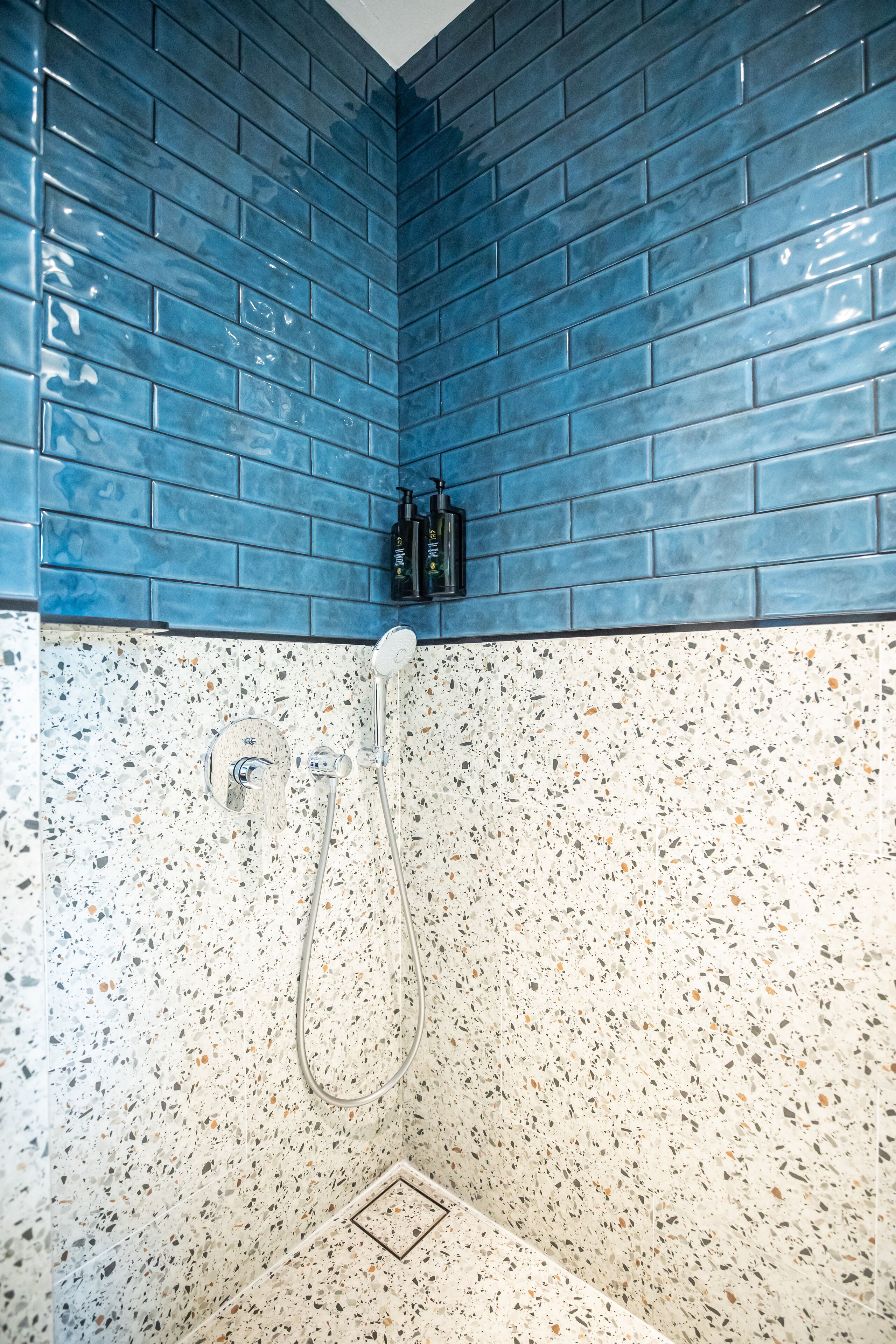 A bathroom with blue tiled walls and a speckled tile floor.