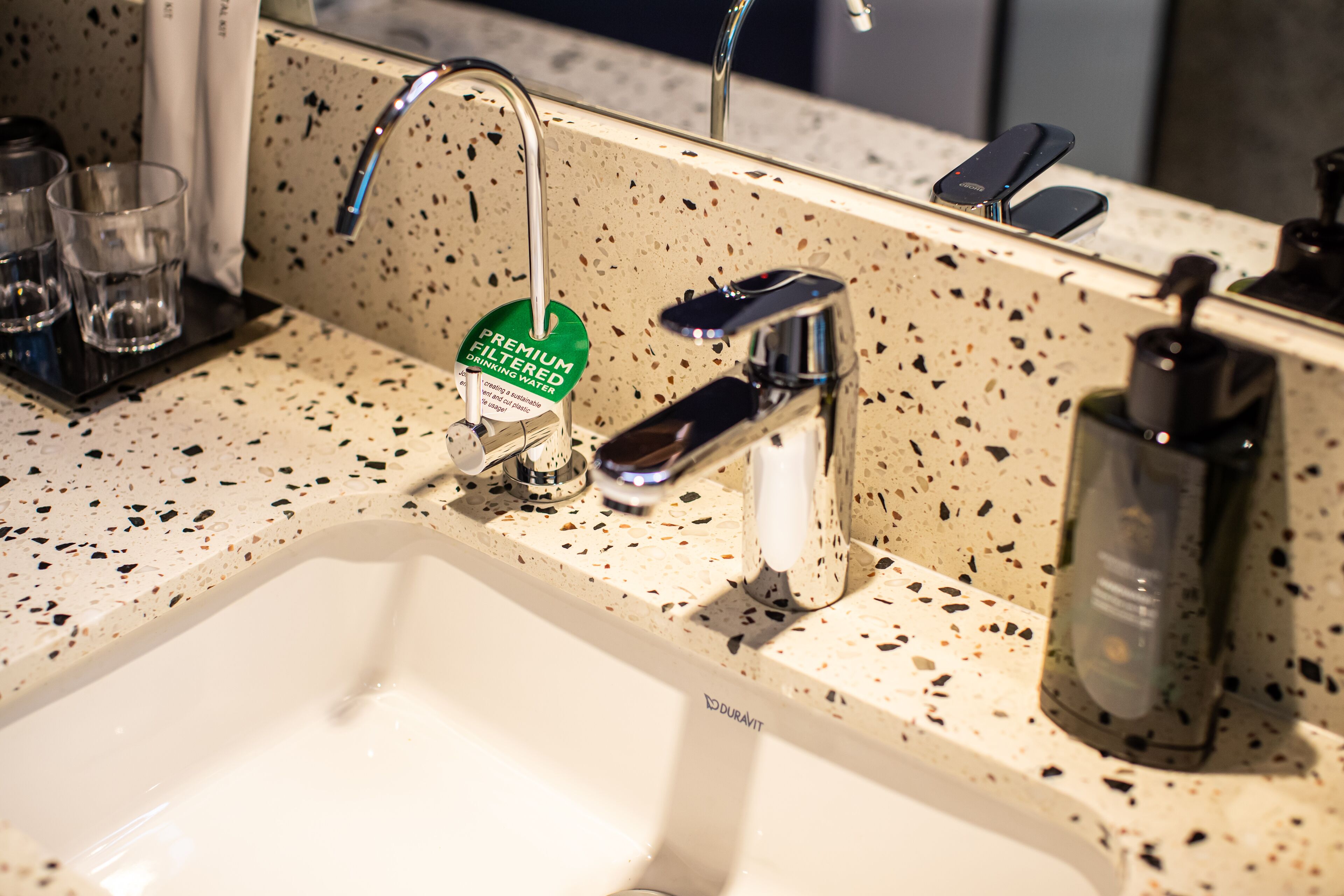 A bathroom sink with a speckled countertop, a mirror, and a bottle of hand soap.