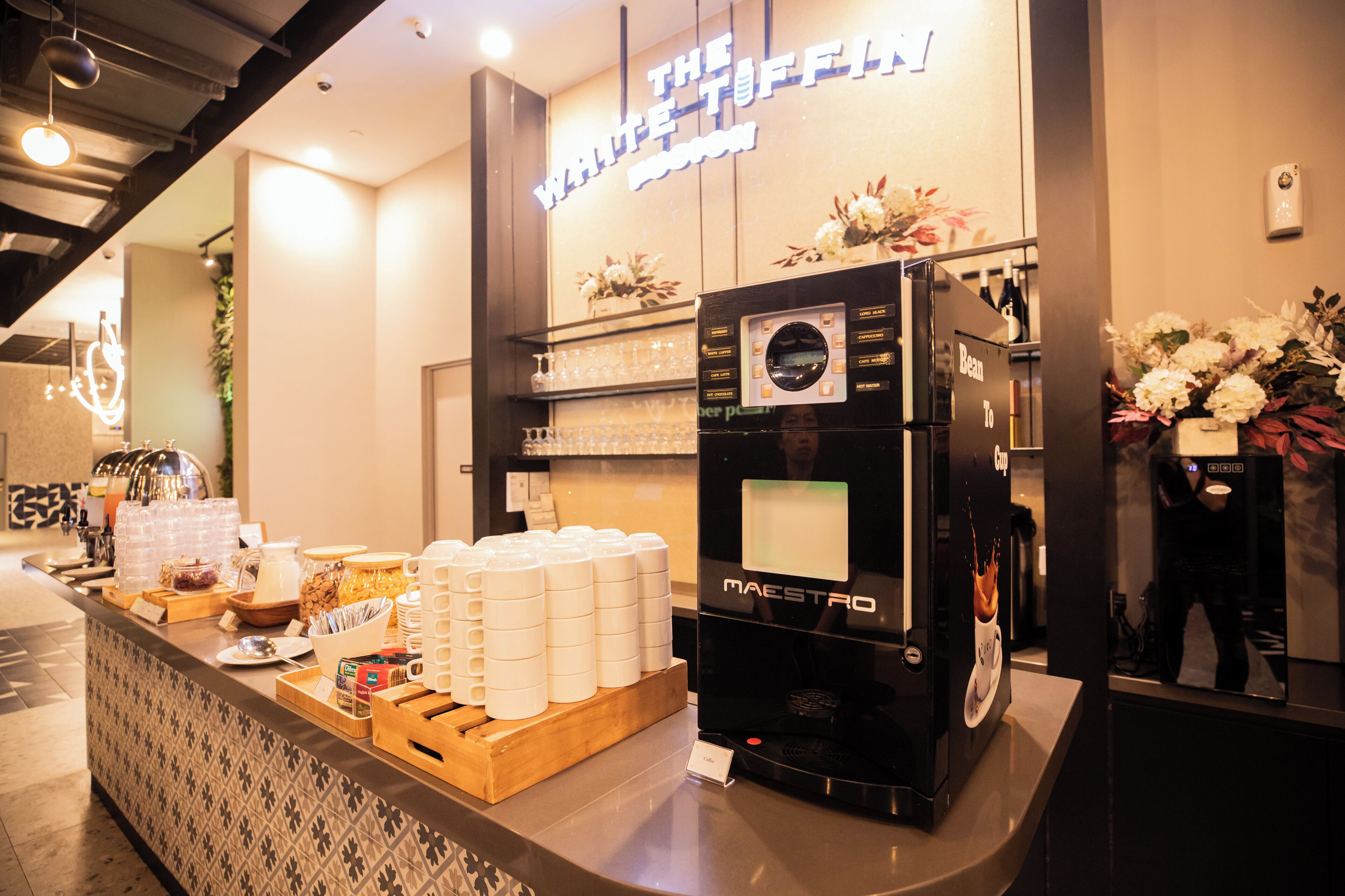 A hotel reception area with a coffee machine, a counter with various items, and a sign that reads "The White Offic".
