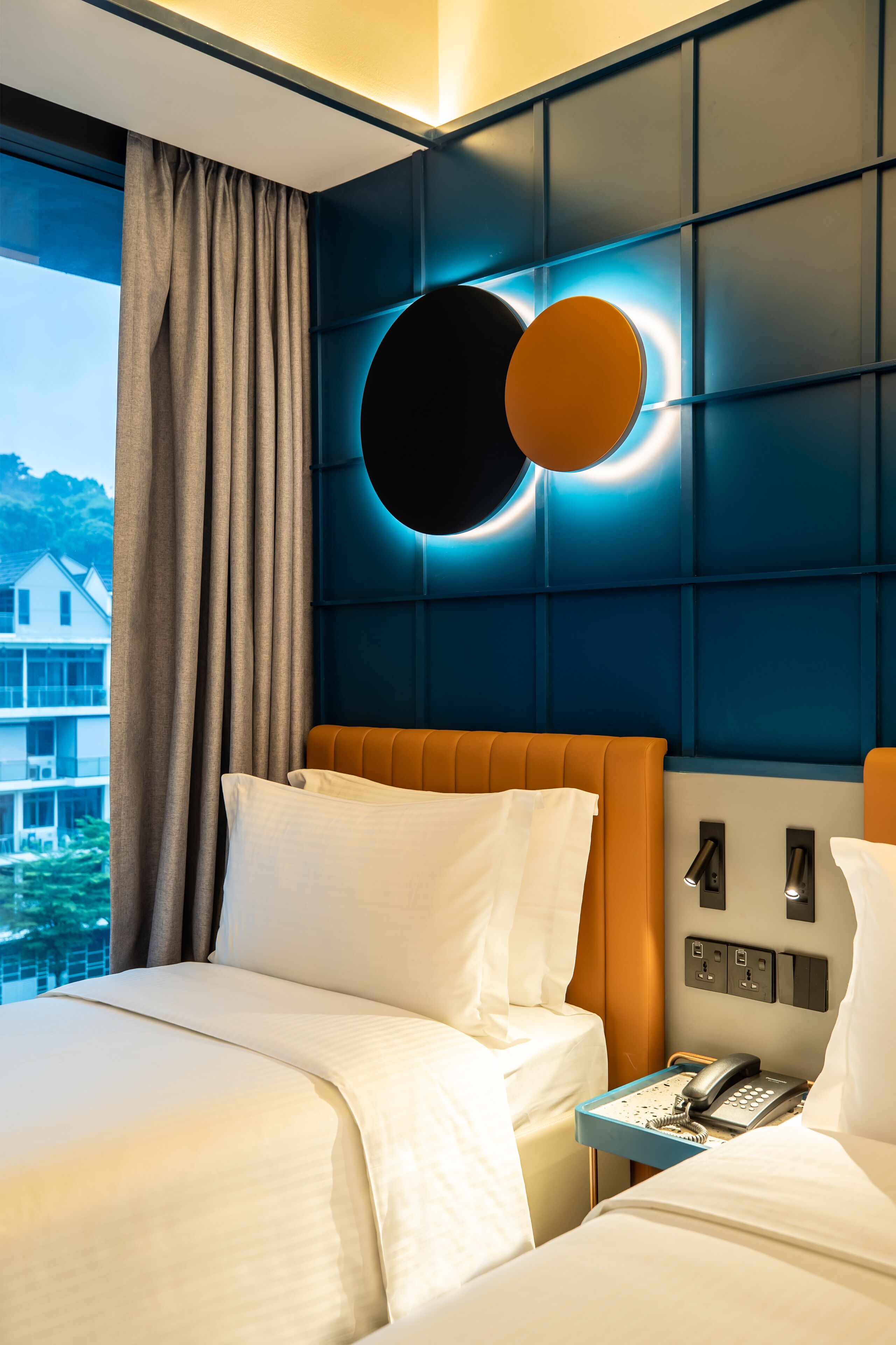 Habitación de hotel con una cama grande, una mesita de noche con teléfono y vista a un edificio.
