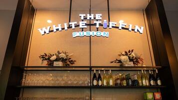 Zona de bar con un letrero que dice 'The White Tiffin Fusion' y estantes llenos de botellas y vasos.