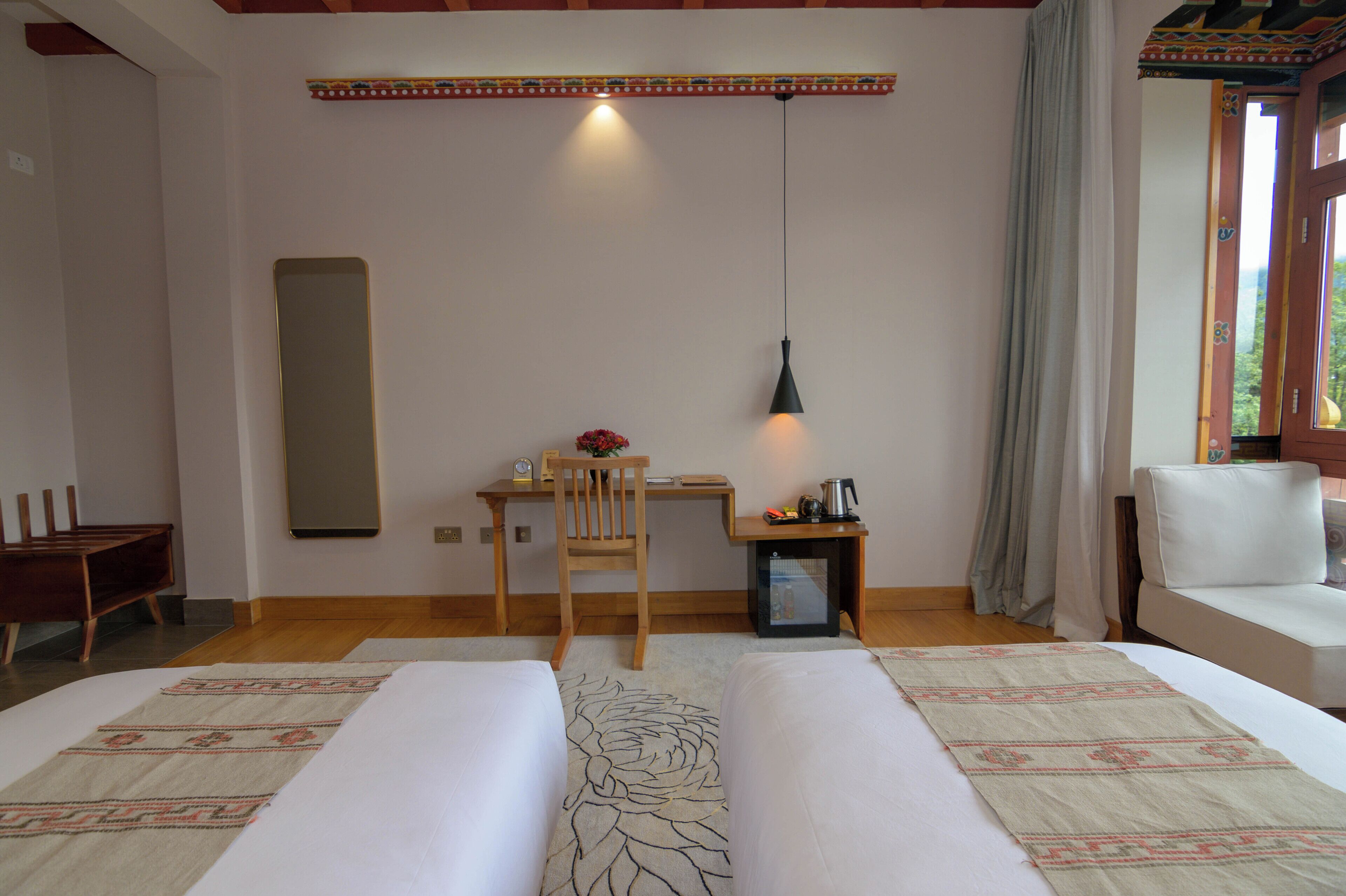 A hotel room with two beds, a desk, a chair, a small table with a lamp, and a sofa.
