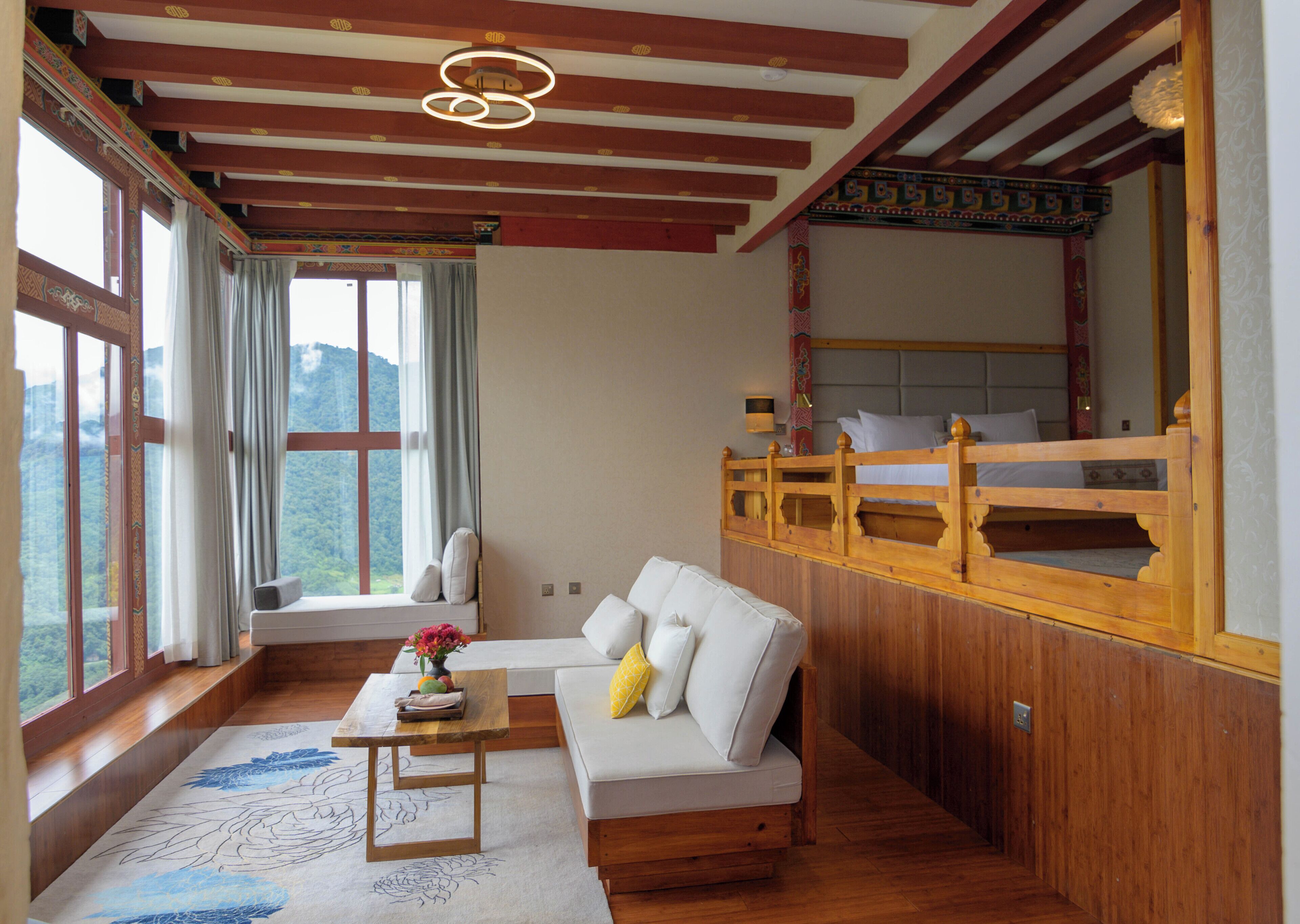 Een kamer met een houten plafond, een bank, een kleine tafel met een vaas en een raam met gordijnen.