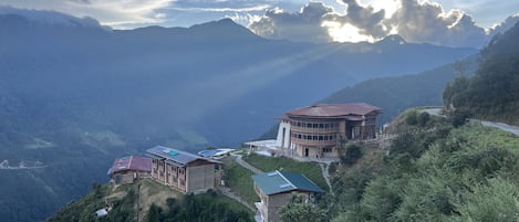 A building with a traditional architectural style, situated on a hillside with a view of surrounding mountains.