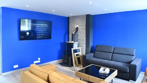 Ein modernes Wohnzimmer mit blauer Akzentwand, einem an der Wand befestigten Flachbildfernseher, einem grauen Sofa, einem Holztisch und einem Kamin.